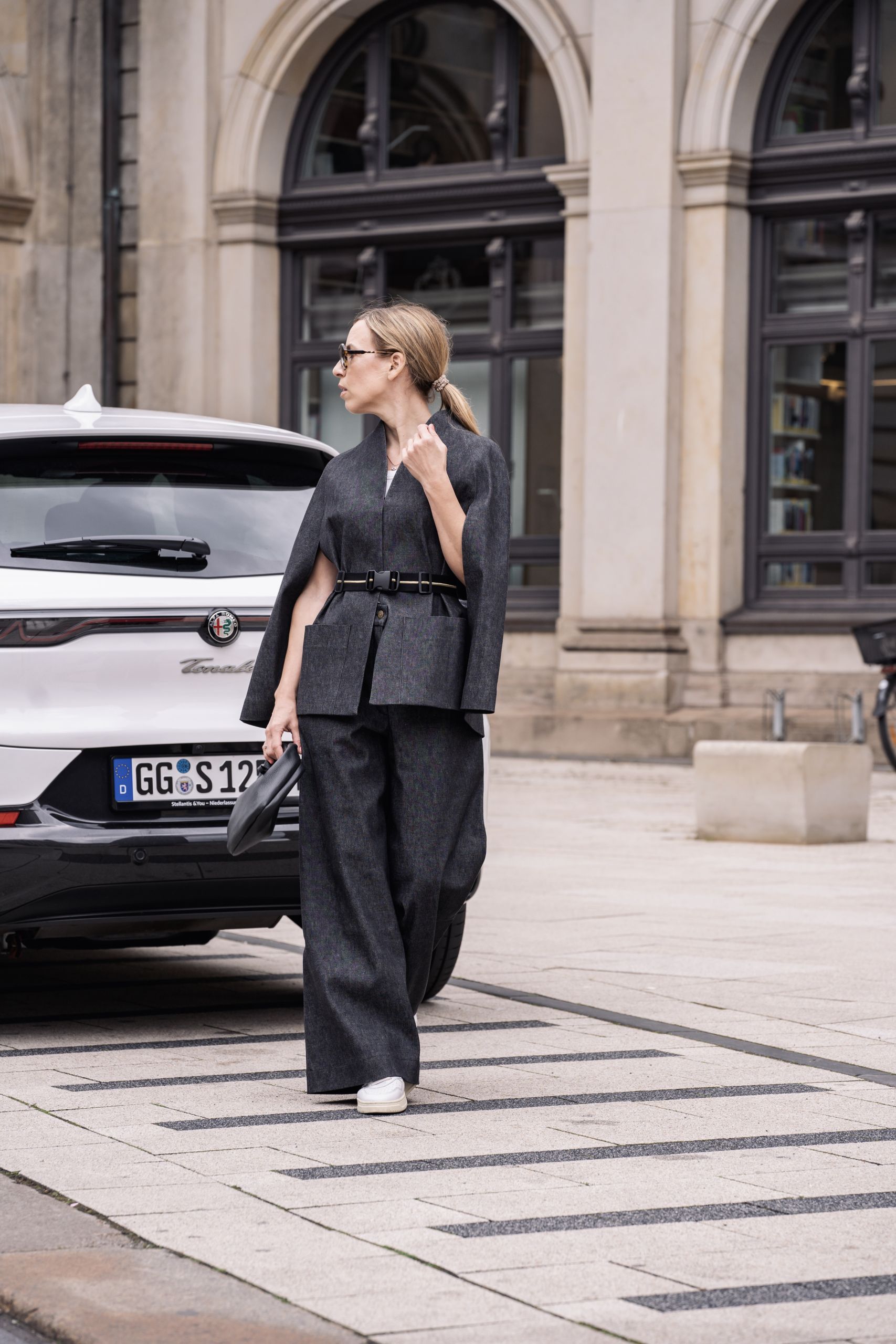 Frau in schwarzem Hosenanzug vor weißem Auto in der Innenstadt von Hamburg